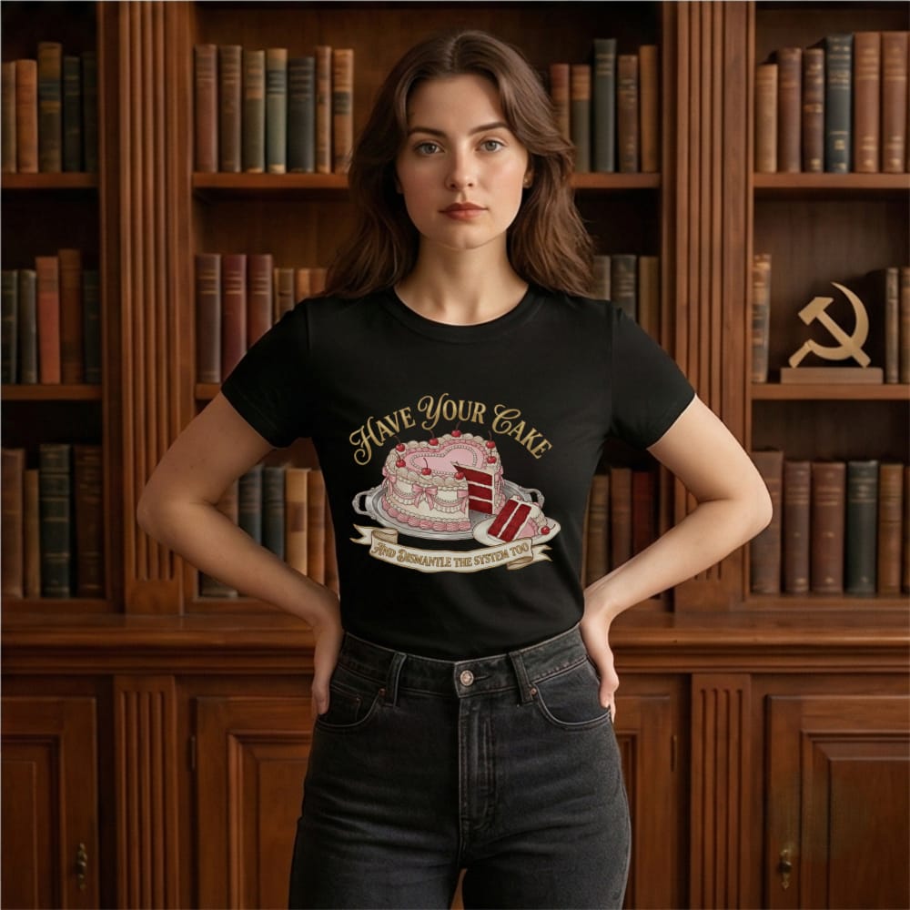 A woman stands confidently in front of a wooden bookshelf filled with books and a hammer-and-sickle symbol. Her black T-shirt reads "Have Your Cake and Dismantle the System Too" with a cake graphic. The setting feels intellectual and bold.
