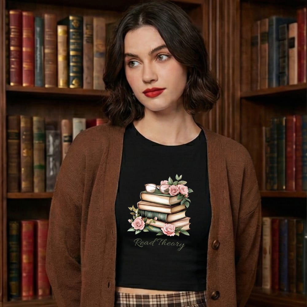Young woman in a cozy library, wearing a brown cardigan and black T-shirt with floral book graphic and the words "Read theory". She has a thoughtful expression, surrounded by bookshelves.